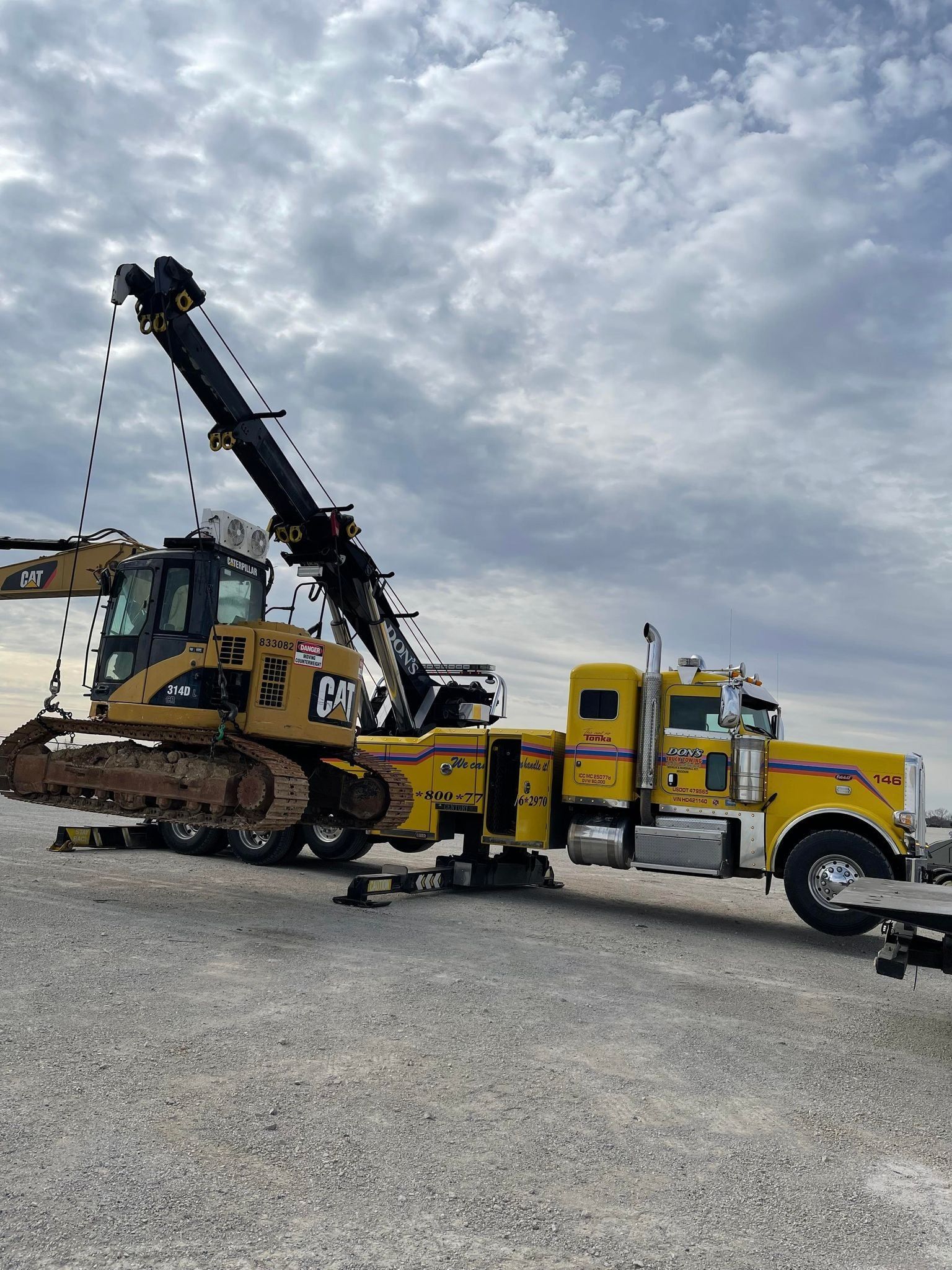Don’s yellow heavy wrecker lifting Caterpillar construction equipment with its boom and outriggers extended